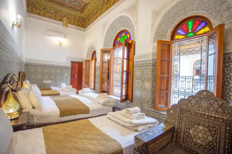 Amplia habitación triple en Riad Fes iline Medina en Fes con ventanas arqueadas, vidrieras de colores y camas perfectamente preparadas