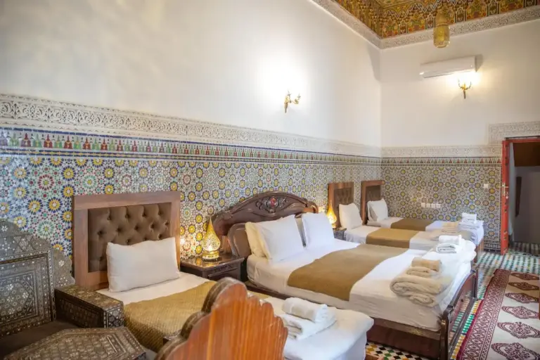 Habitación triple en Riad Fes iline Medina en Fes vista desde la puerta con detalles tradicionales marroquíes y tres camas preparadas