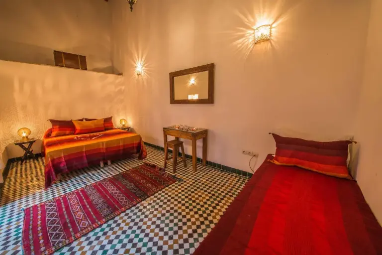 Habitación doble con dos camas en Riad Gzira Fez en Fes con ropa de cama colorida, baldosas estampadas y decoración tradicional