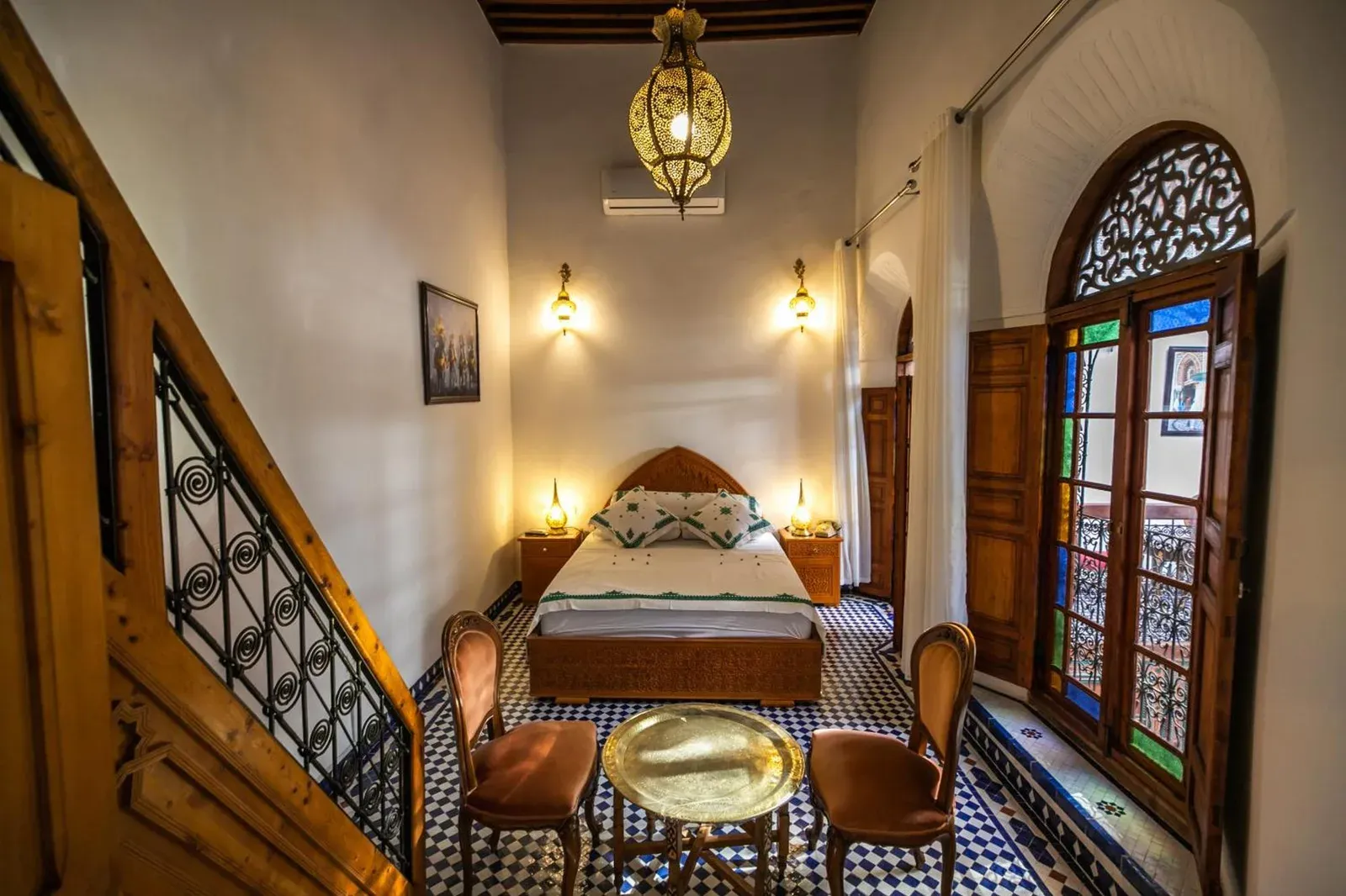 Habitación de huéspedes en Riad Jamal en Fes con una cama doble, puertas de vidrieras y suelo de baldosas marroquíes con motivos.