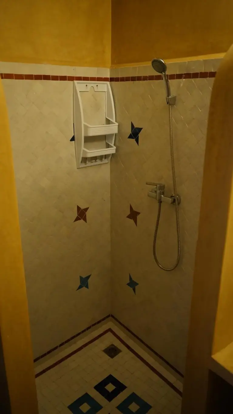 Zona de ducha alicatada en Riad Jamal en Fes con un cabezal de ducha montado en la pared y detalles de baldosas marroquíes en forma de estrella.