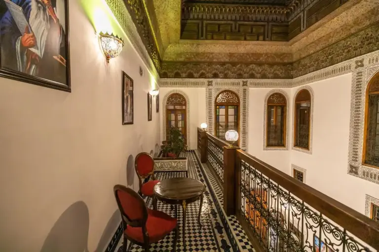 Galería superior en Riad Jamal en Fes con arcos ornamentados, detalles decorativos en el techo y asientos a lo largo del pasillo.