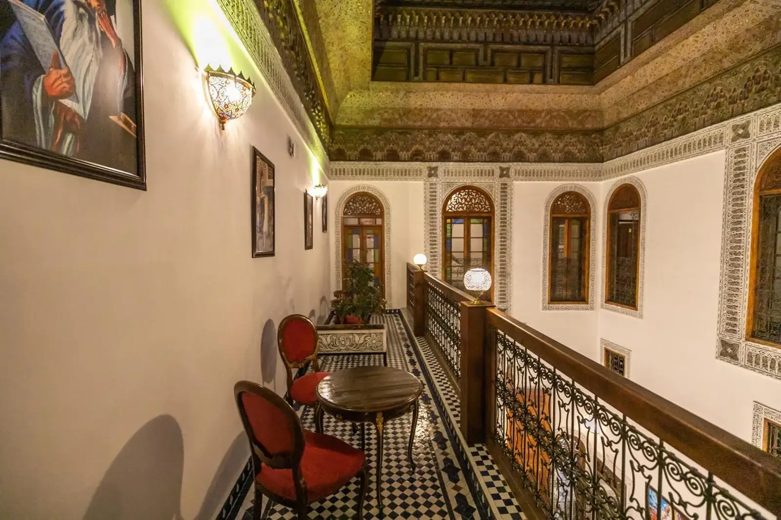 Galería superior en Riad Jamal en Fes con arcos ornamentados, detalles decorativos en el techo y asientos a lo largo del pasillo.