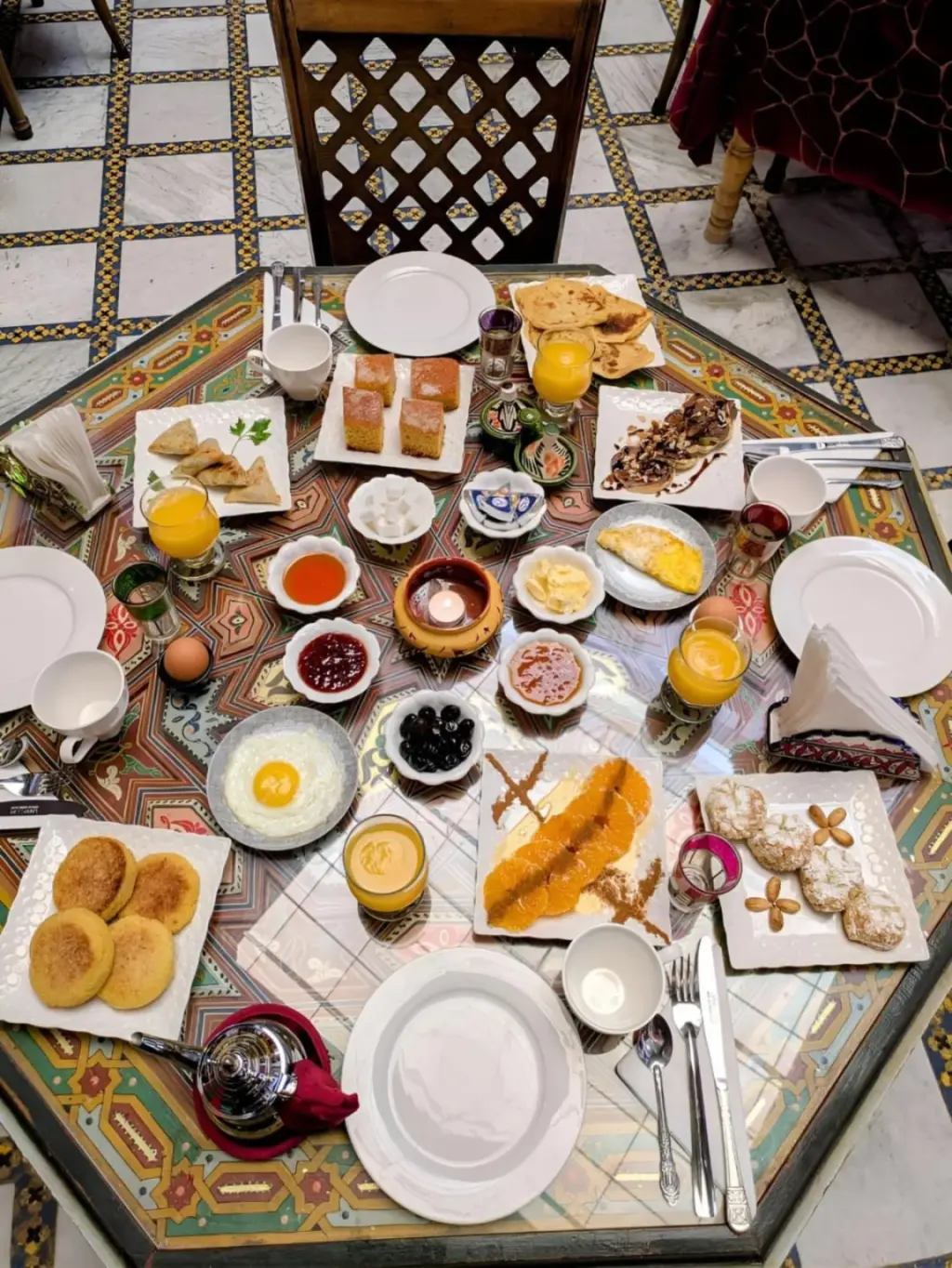 Mesa de desayuno en Riad Lhaj Luxury Palace en Fes con bollería, huevos, zumo y una mesa de estilo marroquí