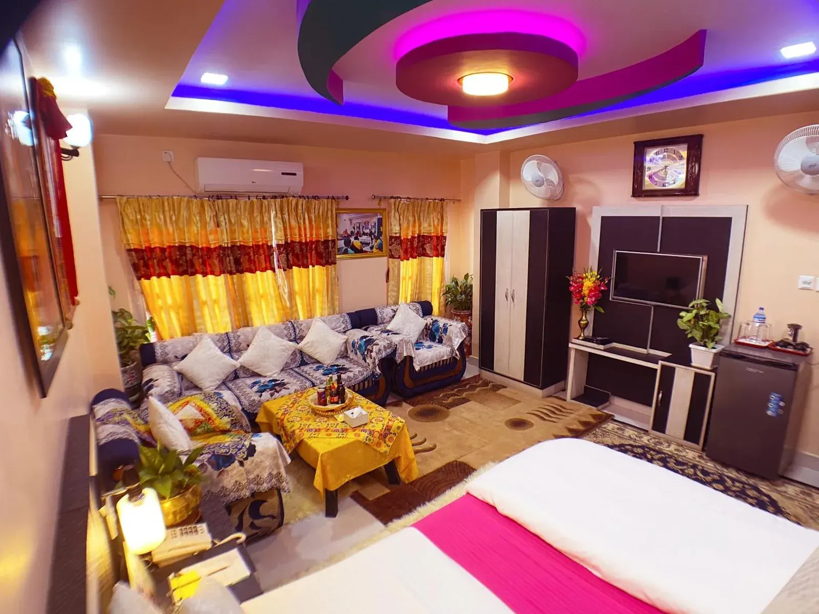 Intérieur d’une suite au RINGJI PALACE à Birtamod avec coin salon, espace TV et éclairage décoratif au plafond.