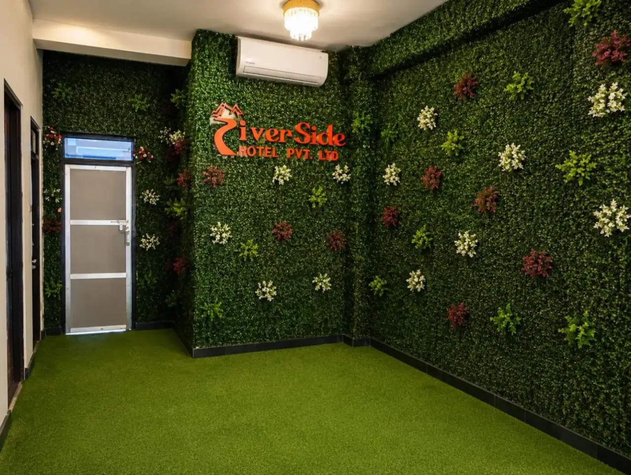 Zona de vestíbulo de temática verde en River Side Hotel Pvt Ltd en Bandipur con plantas decorativas en la pared y suelo de césped artificial