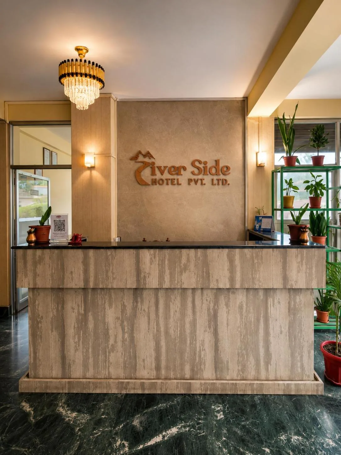 Mostrador de recepción en River Side Hotel Pvt Ltd en Bandipur con letrero de marca y plantas de interior