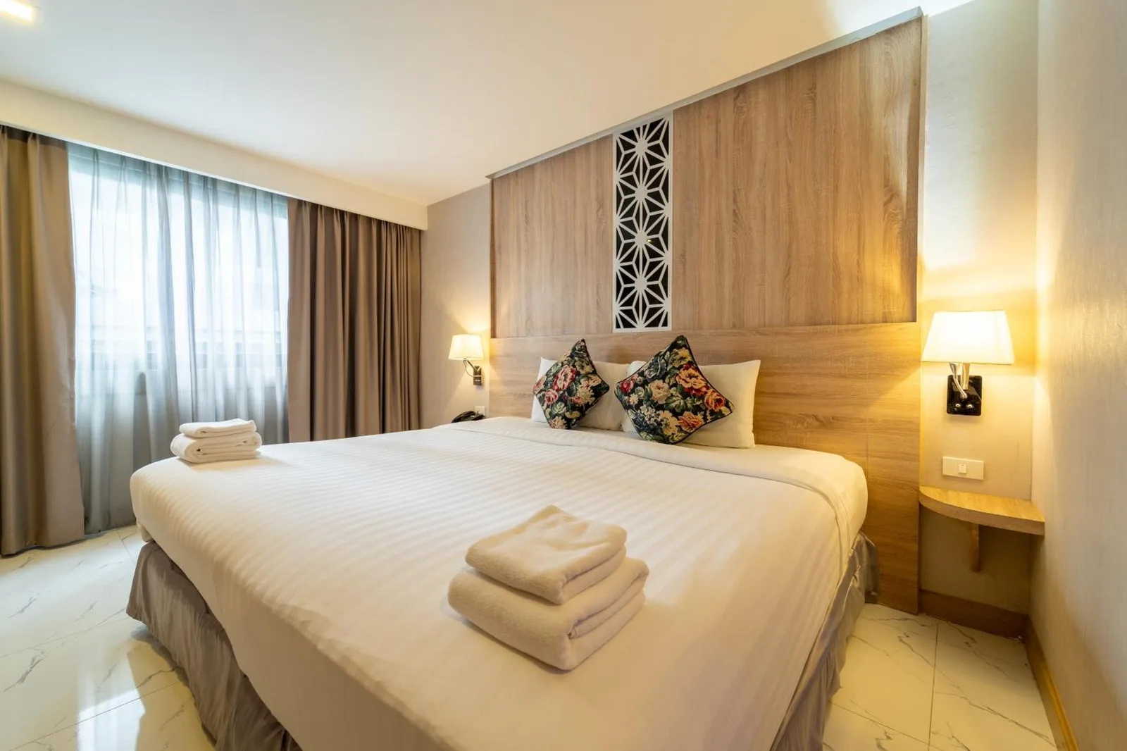 Rodina Beach Hotel Pattaya guest room with king bed, bedside lamps, and large window curtains