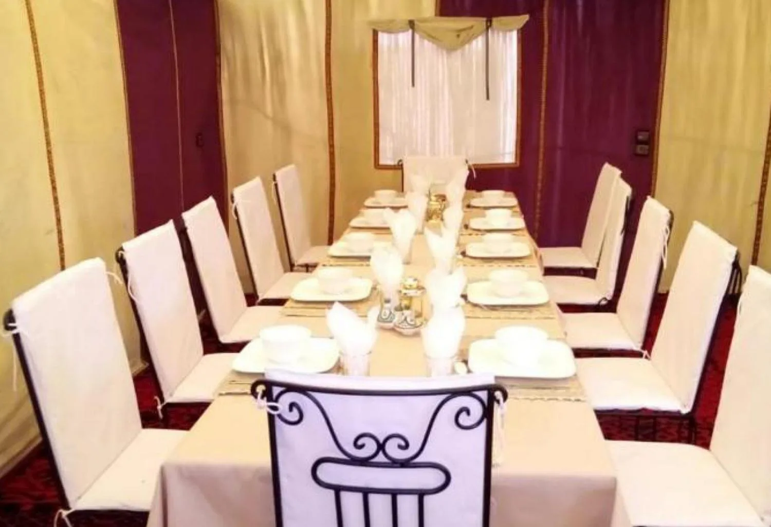 Roses desert camp in Merzouga banquet-style dining table with white chairs and formal place settings