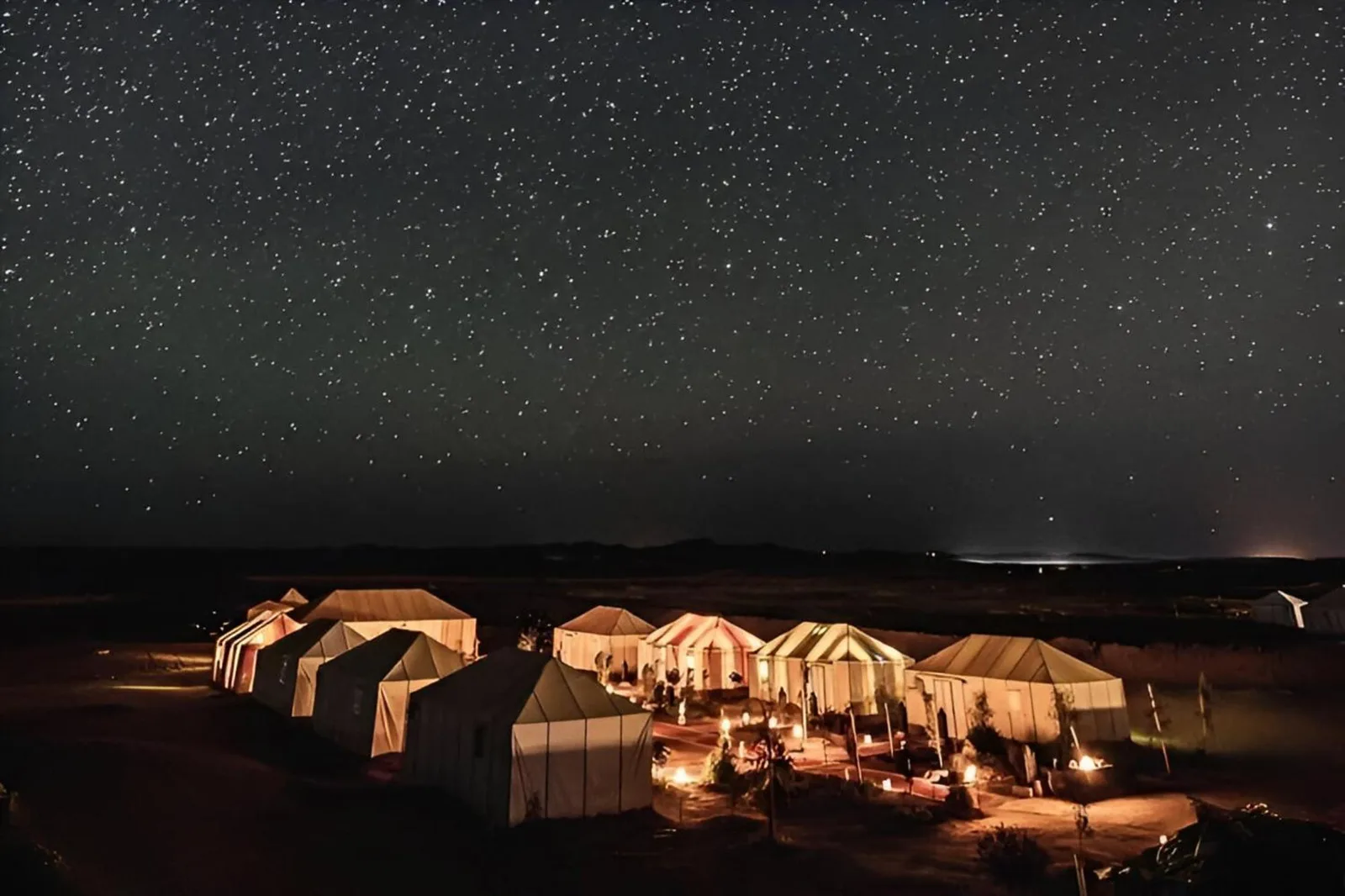 Roses desert camp in Merzouga illuminated at night under a star-filled Sahara sky
