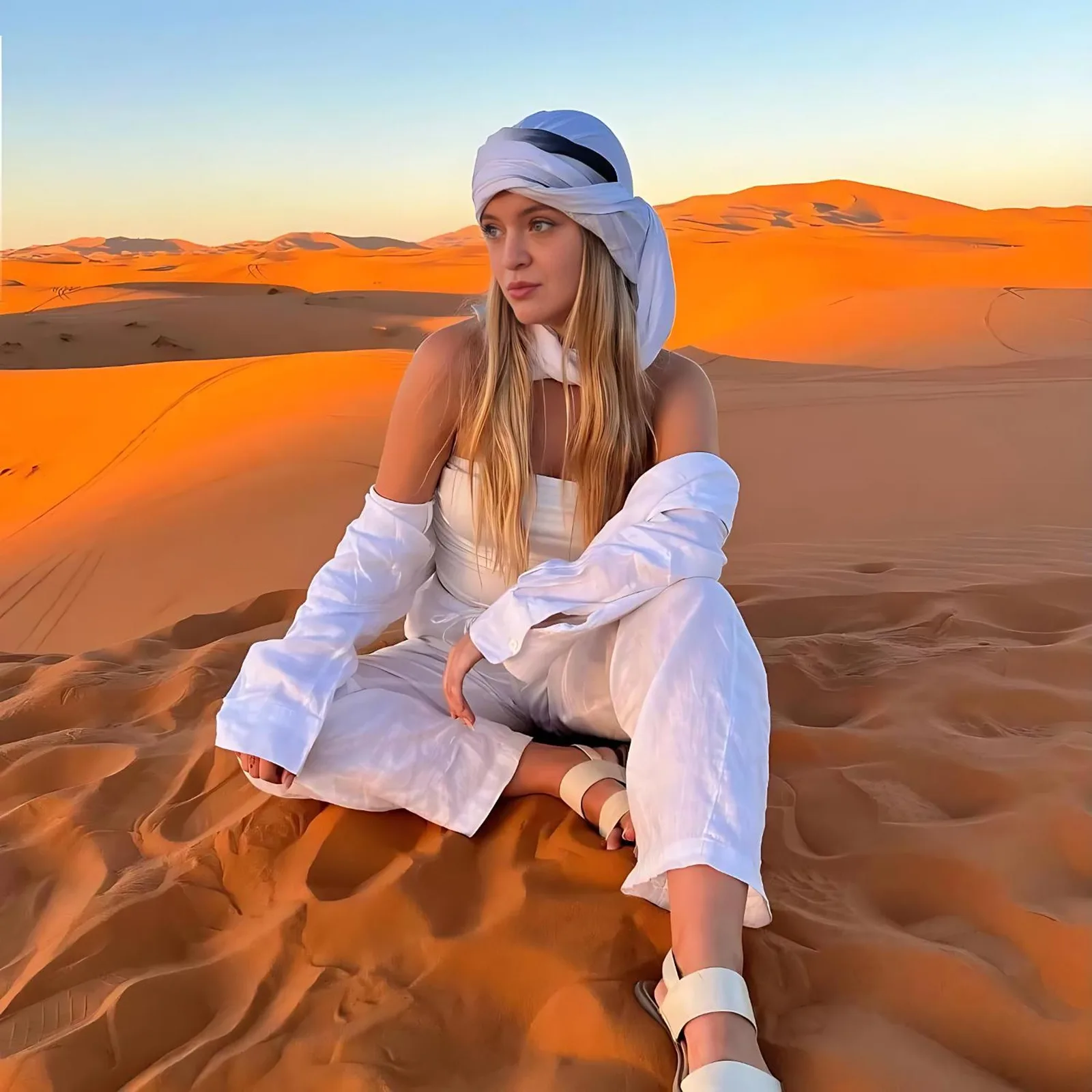 Woman sitting on Sahara dunes near Roses desert camp in Merzouga at golden hour