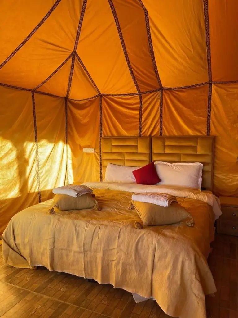 Comfortable double bed in a luxury tent at Safari Desert Camp in Merzouga with pillows and folded towels