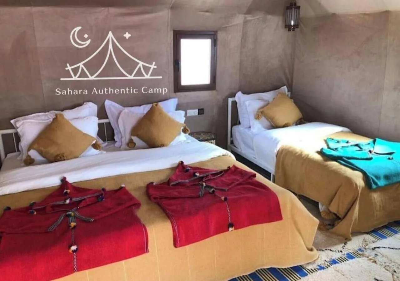 Habitación triple en Sahara Authentic Camp en Merzouga con tres camas, decoración cálida y mantas de colores.