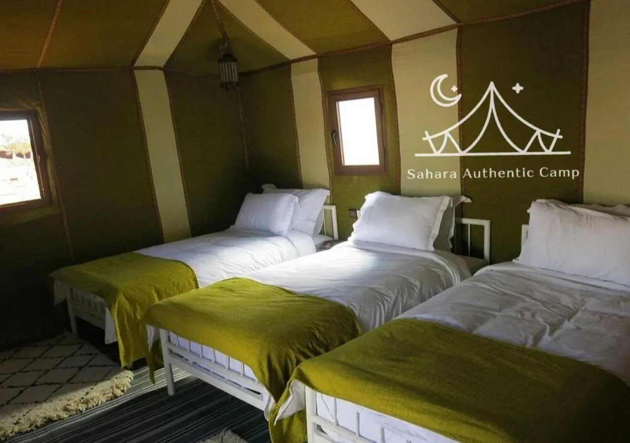 Habitación triple en tienda en Sahara Authentic Camp en Merzouga con ropa de cama verde oliva y paredes panorámicas de la tienda.