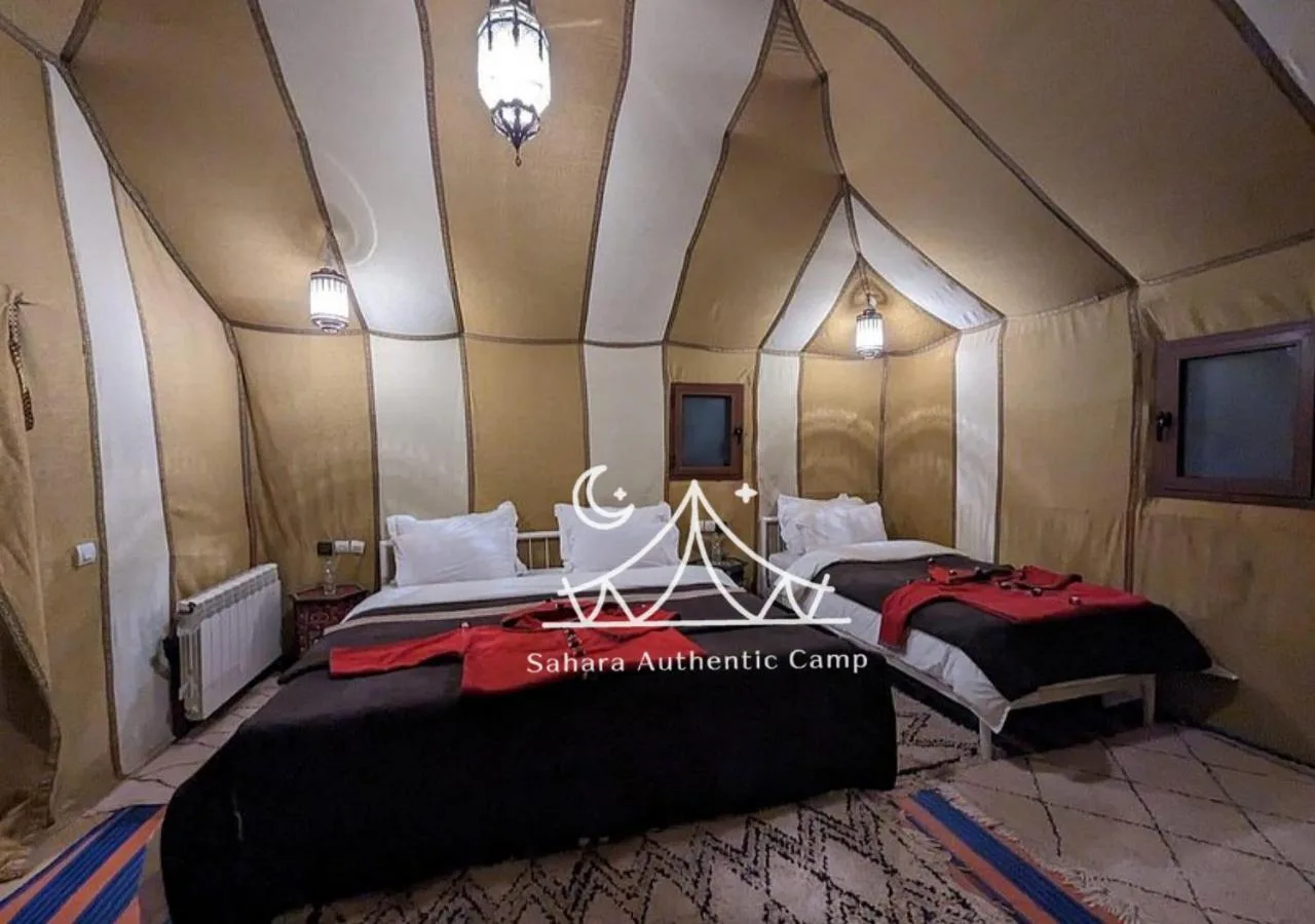 Habitación doble con dos camas en tienda en Sahara Authentic Camp en Merzouga con alfombras tradicionales y una entrada de tienda.