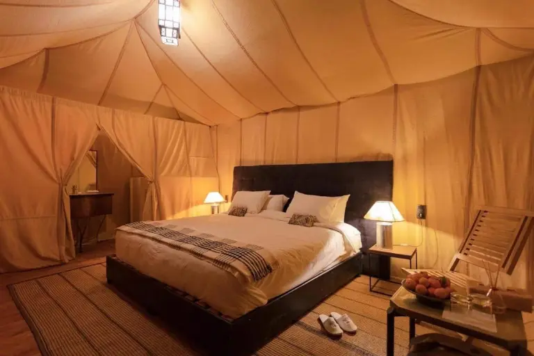 Deluxe guest tent bedroom at Sahara Elegance Camp in Merzouga with a large bed, warm lighting, and elegant desert furnishings