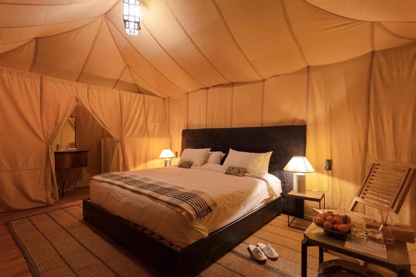 Deluxe guest tent bedroom at Sahara Elegance Camp in Merzouga with a large bed, warm lighting, and elegant desert furnishings