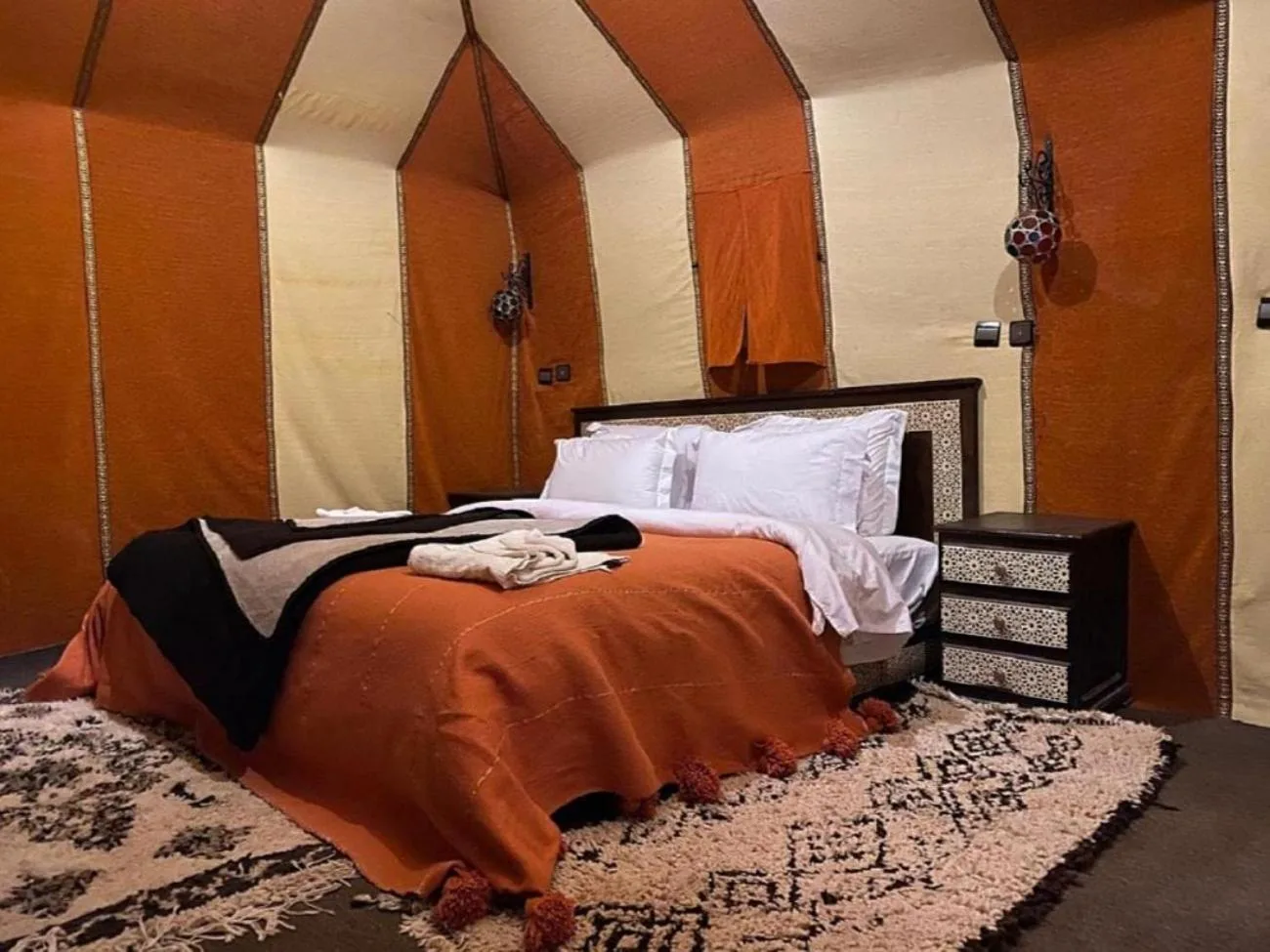 Double guest tent at Sahara Elegance Camp in Merzouga with patterned rugs, a bed, and a side table