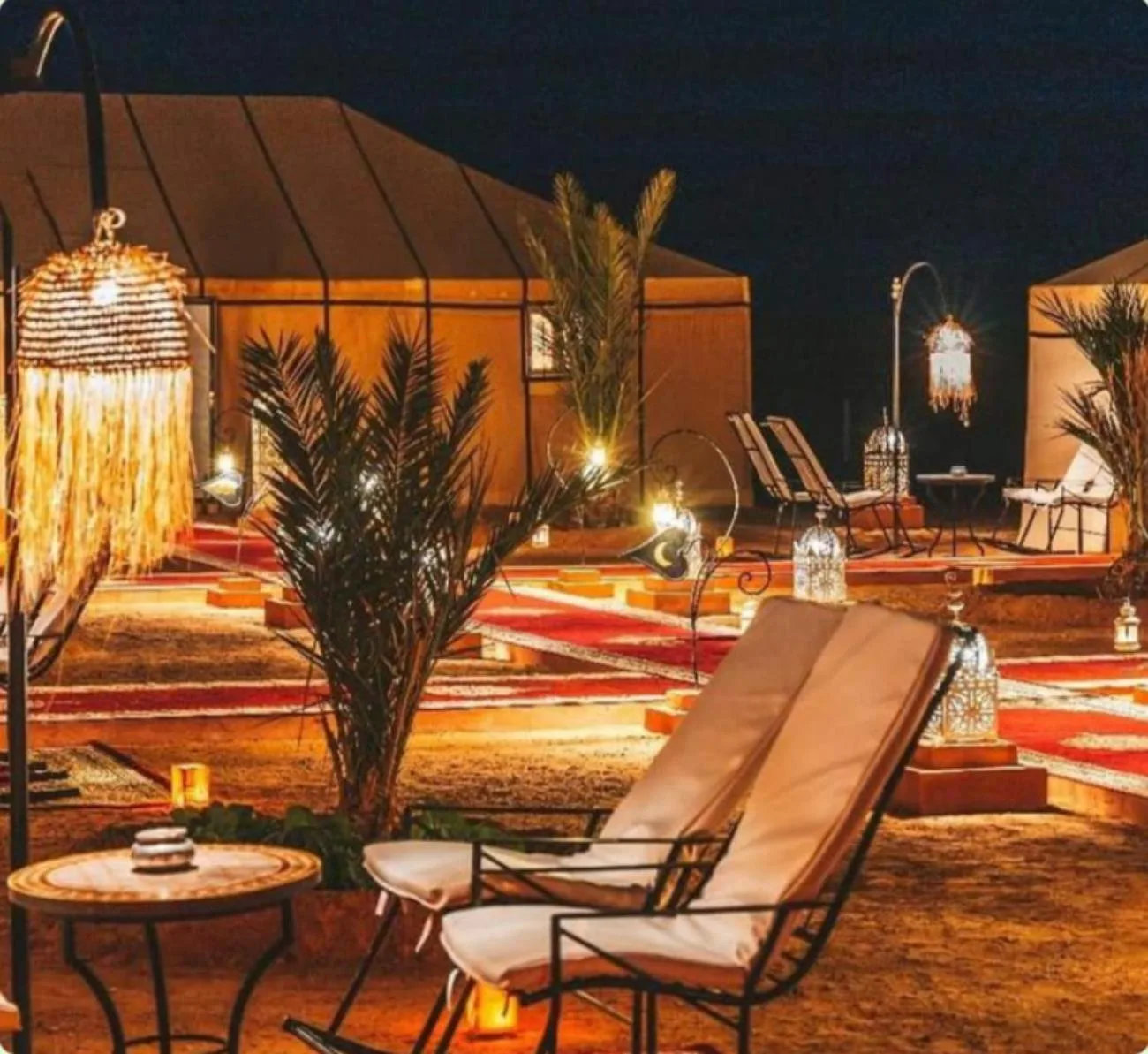 Exterior lounge area at Sahara Elegance Camp in Merzouga with desert seating, lanterns, and illuminated pathways