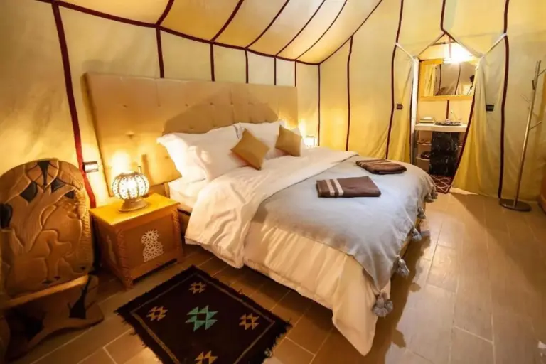 Luxury tent bedroom at Sahara Elegance Camp in Merzouga with a tufted headboard, soft bedding, and decorative accents