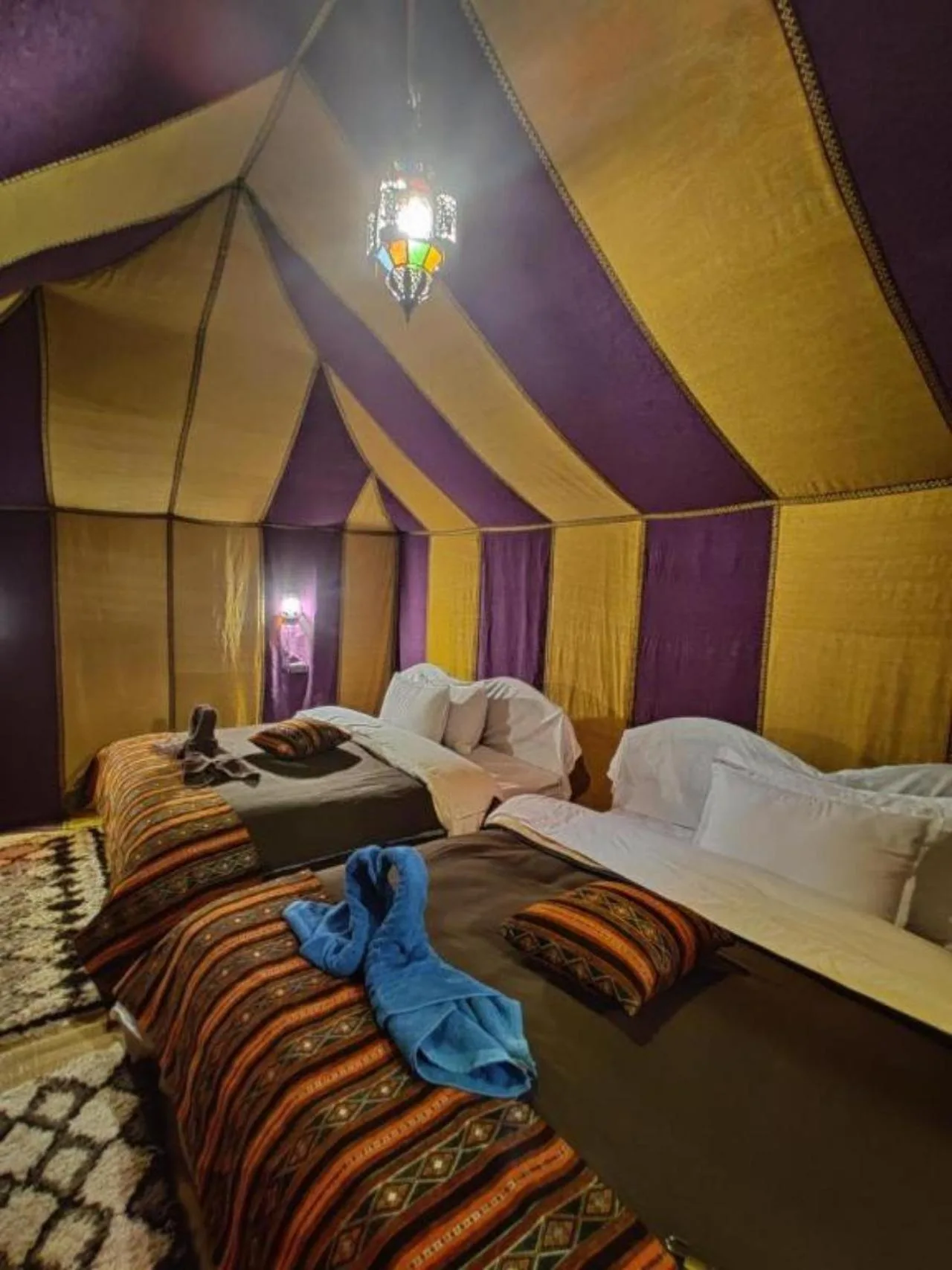 Shared tent room at Sahara Elegance Camp in Merzouga with twin beds, striped bedding, and lantern lighting