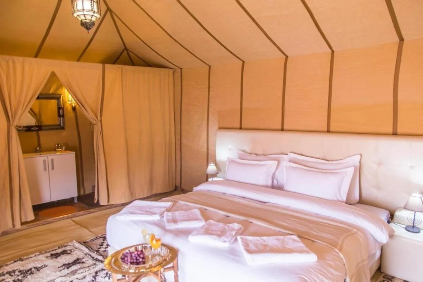 Comfortable tent bedroom at Sahara Elegance Camp in Merzouga with a large bed, side tables, and private ensuite access