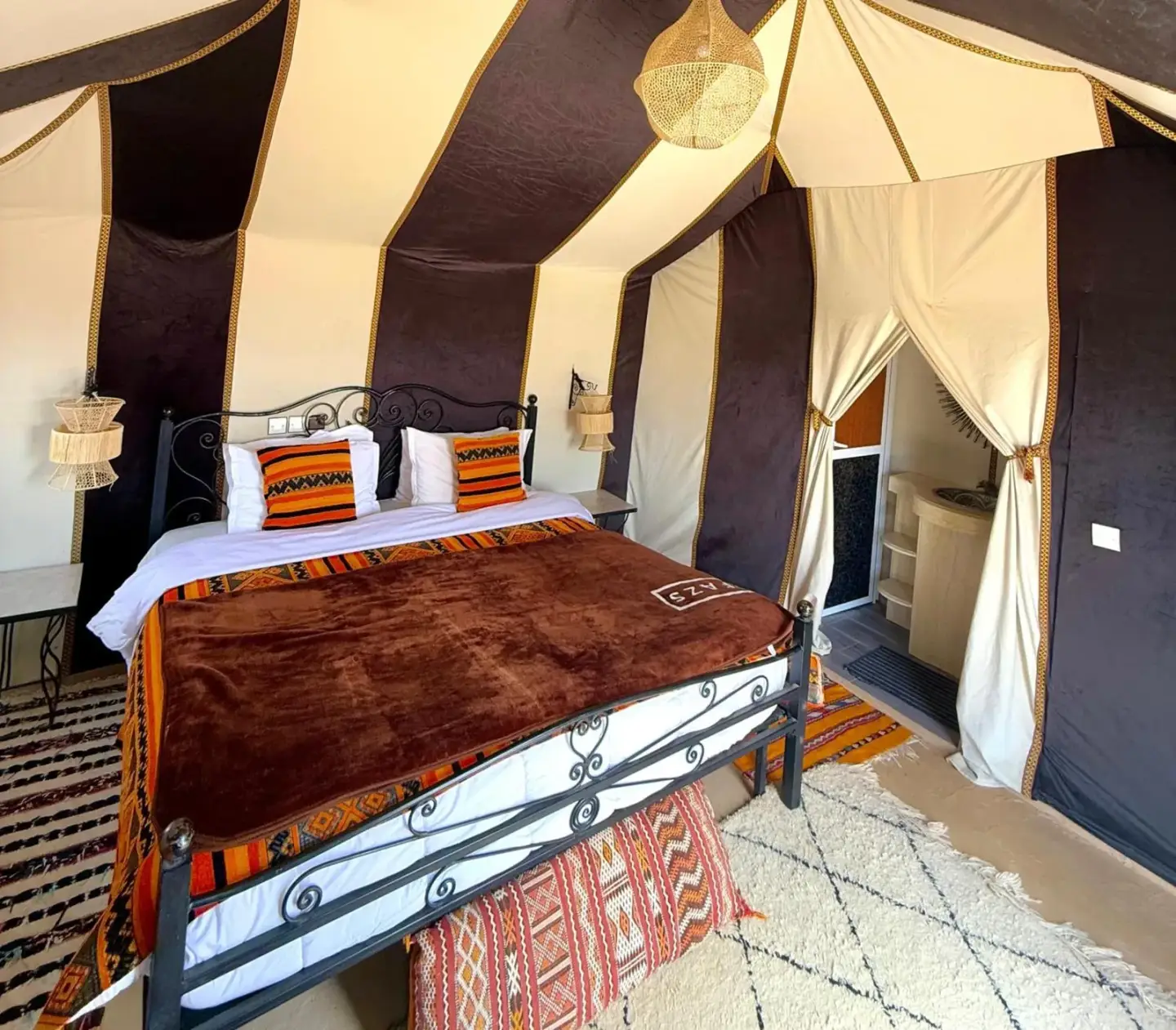 Interior de una tienda de lujo en Sahara Family Luxury Camp en Merzouga con una cama, decoración tradicional y acceso a baño privado.