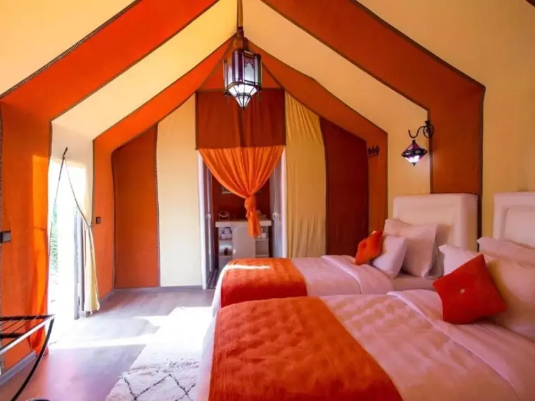 Tienda dormitorio con dos camas en Sahara Family Luxury Camp en Merzouga, con detalles en naranja y una lámpara colgante.