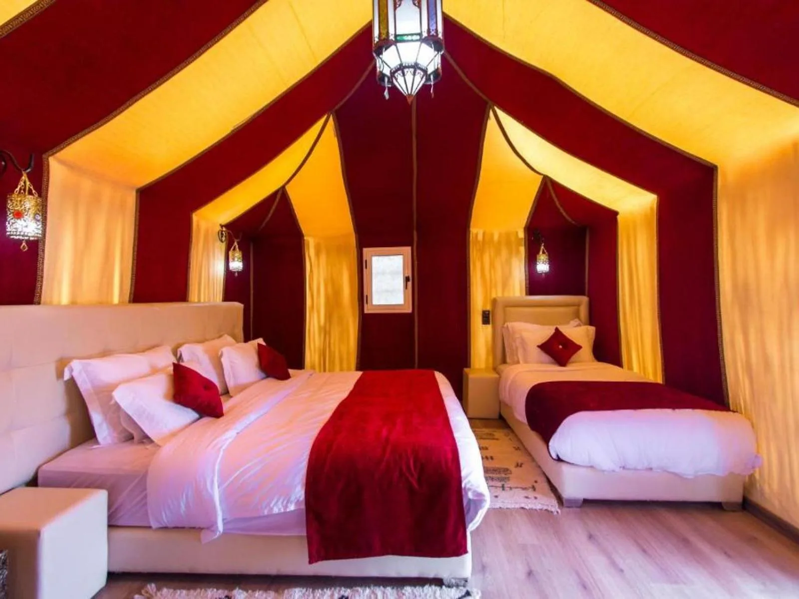 Interior de una tienda de lujo con dos camas en Sahara Family Luxury Camp en Merzouga, con decoración cálida en rojo y dorado.