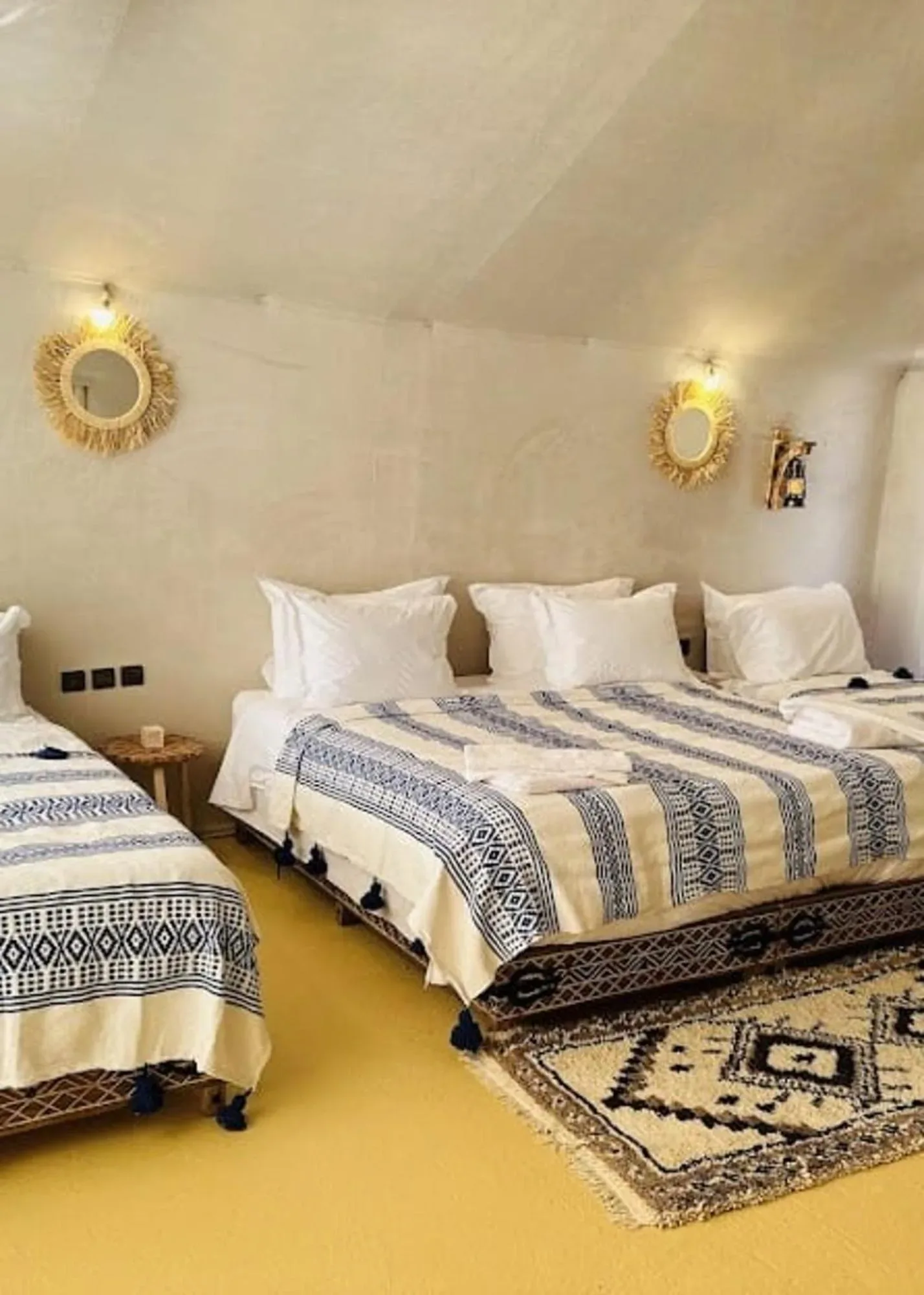 Twin tent room at Sahara Luxe Camp in Merzouga with three beds, patterned blankets, and desert camp decor.