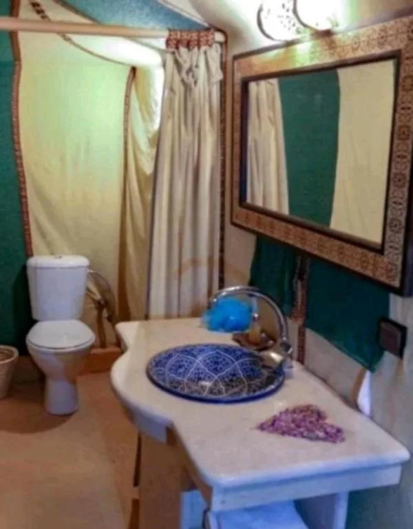 Bathroom vanity inside Sahara Relax Camp in Merzouga with sink, mirror, toilet, and shower curtain