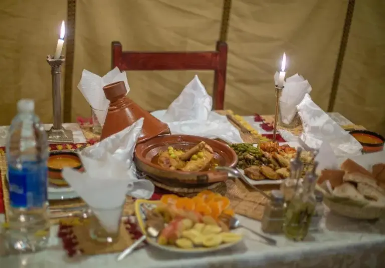 Dining table setup at Sahara Relax Camp in Merzouga with Moroccan dishes, candles, and fruit
