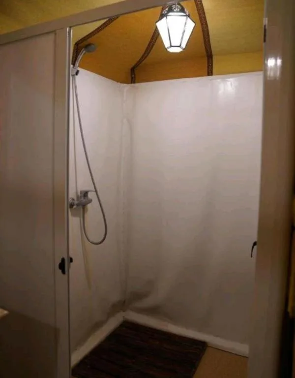 Private shower stall at Sahara Relax Camp in Merzouga with white walls and overhead lantern light