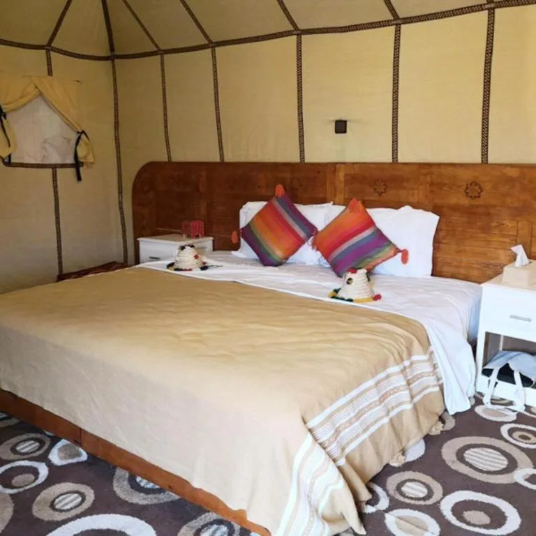Standard tent room at Sahara Relax Camp in Merzouga with a large bed, colorful pillows, and bedside tables