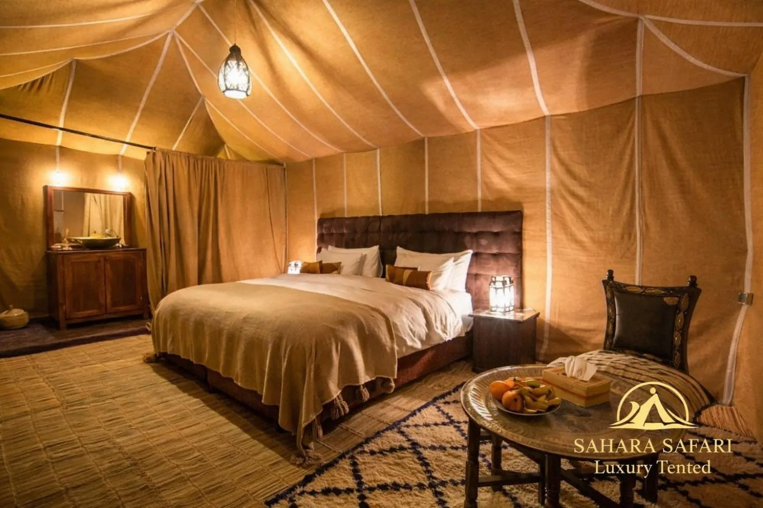 Luxus-Zelt-Schlafzimmer im Sahara Safari Luxury Camp & Activities in Merzouga mit Kingsize-Bett, warmem Licht und traditioneller Einrichtung.