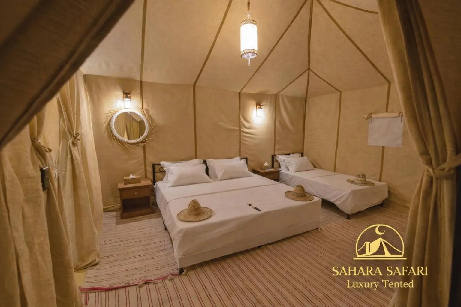 Innenraum eines Zwillingsbett-Zelts im Sahara Safari Luxury Camp & Activities in Merzouga mit schlichter Einrichtung und warmem Umgebungslicht.