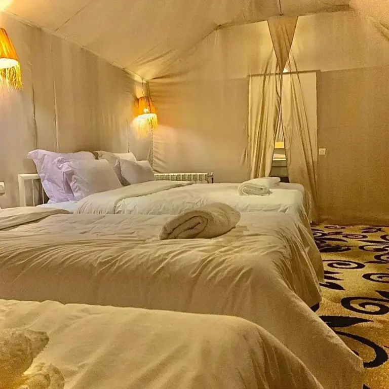 Sahara Soul Luxury Camp in Merzouga family tent room with multiple beds and plush white bedding.
