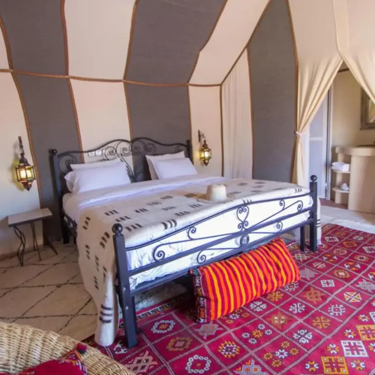 Spacious bed and colorful decor inside Sahara Tours luxury camp in Merzouga