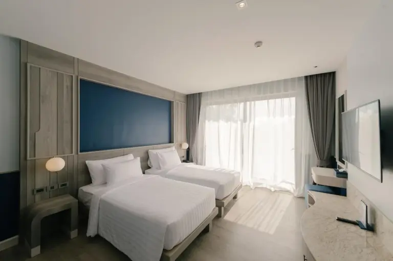 Chambre twin au Seabed Grand Hotel Phuket à Phuket avec grandes fenêtres, rideaux et mobilier moderne.