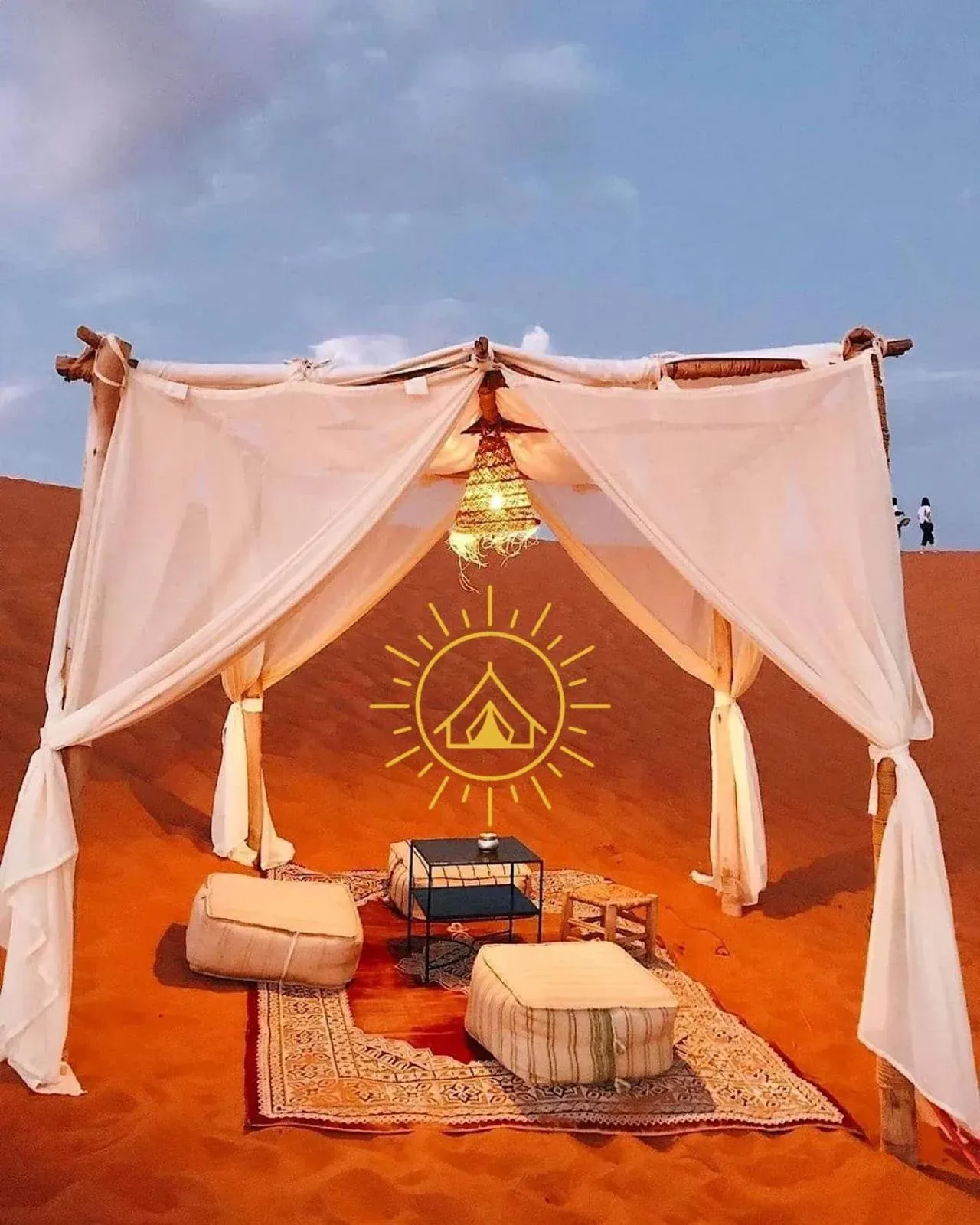 Desert lounge setup at Shining Luxury Camp in Merzouga with draped canopy, rugs, and low seating on the sand