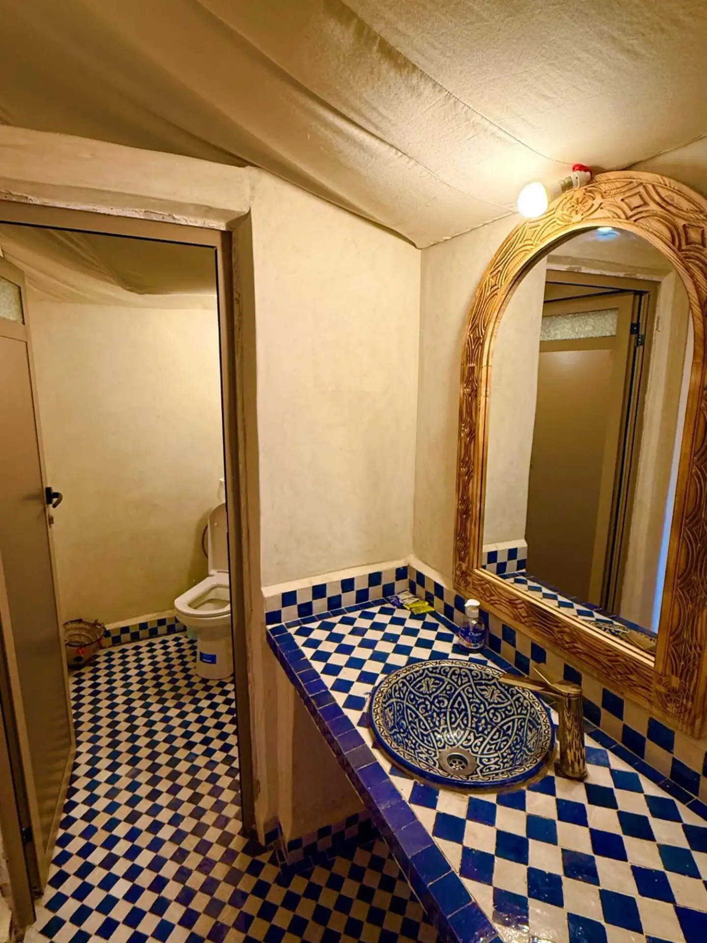 Waschbeckenbereich im Badezimmer des Sinbad Merzouga Camp mit blau-weißen Fliesen und kunstvollem Spiegel in Merzouga