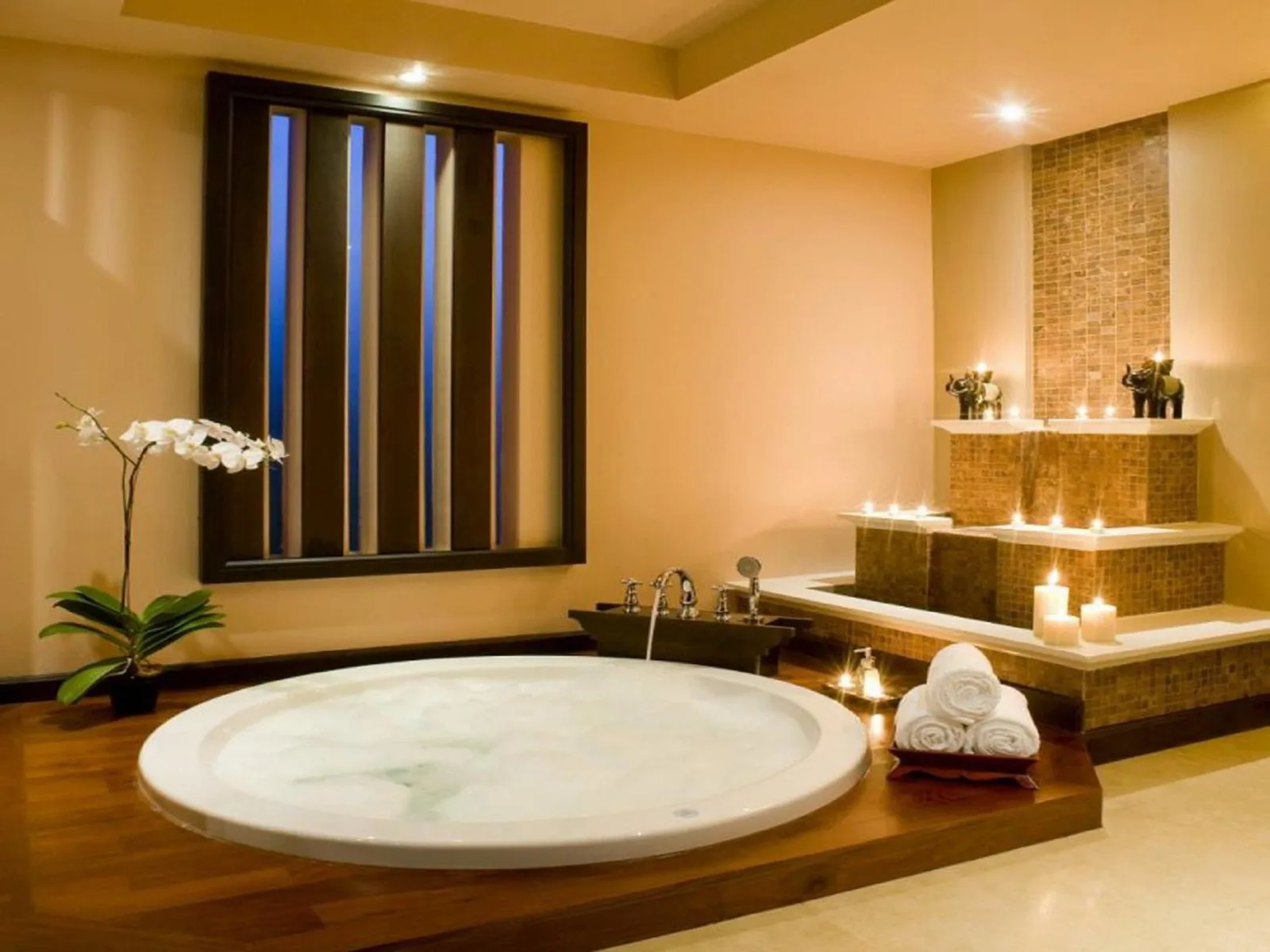 Baño de estilo spa en Siripanna Villa Resort & Spa Chiang Mai -SHA Extra Plus con una bañera redonda de inmersión y escalones iluminados con velas.