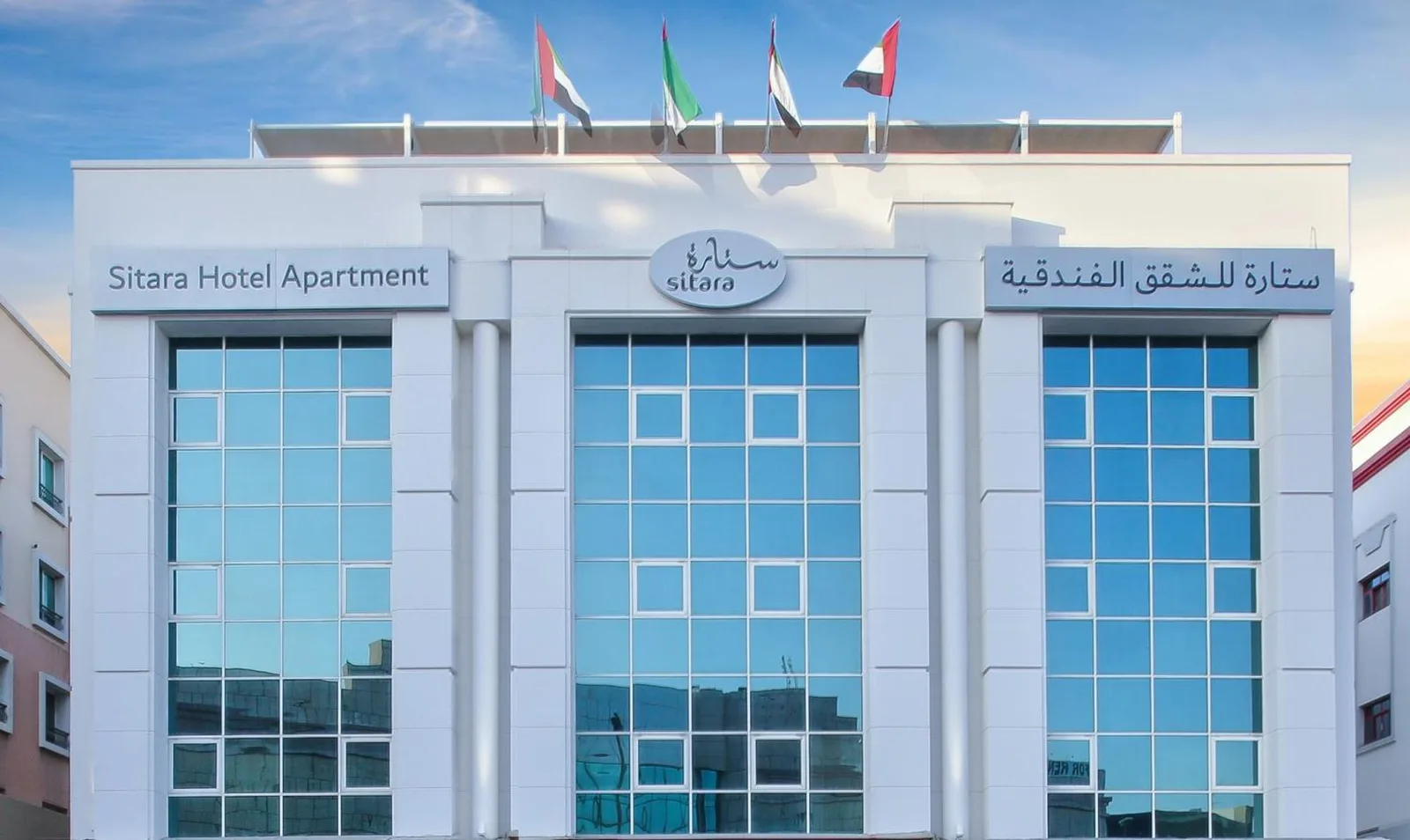 Vue extérieure de Sitara Hotel Apartment à Dubaï avec façade moderne en verre et drapeaux sur le toit