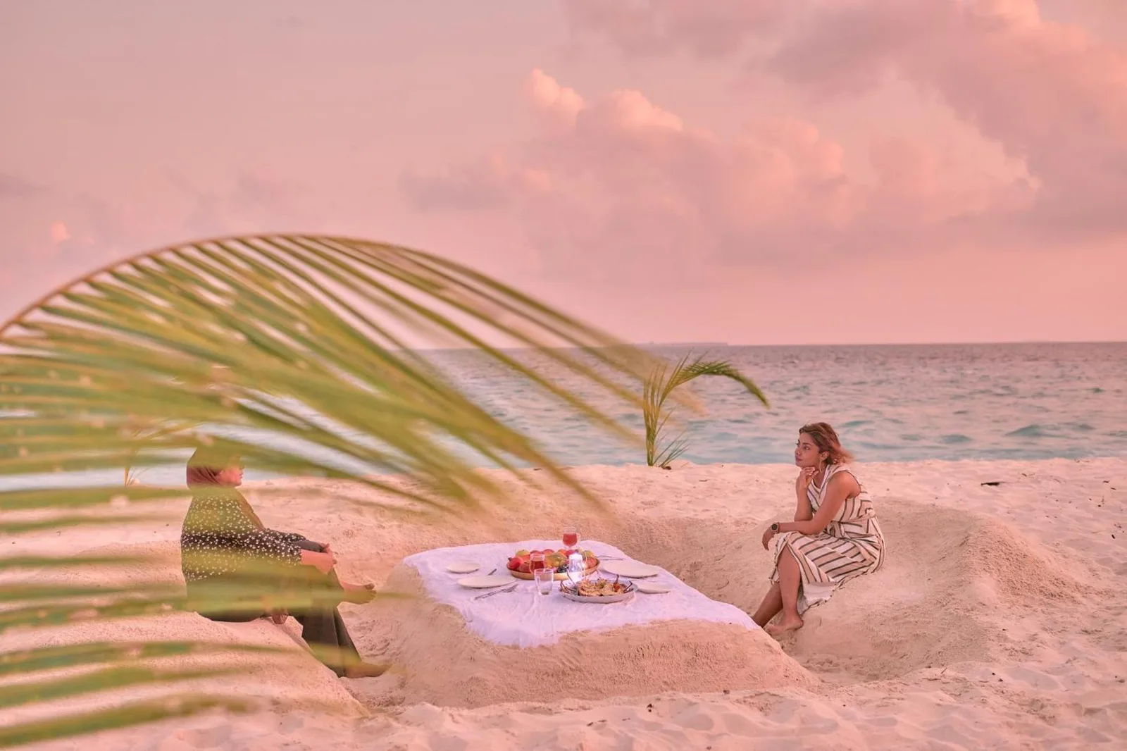 Strand-Dinner-Arrangement im Splendour Grand im Ari-Atoll mit einem romantischen Tisch im Sand am Meer bei Sonnenuntergang.