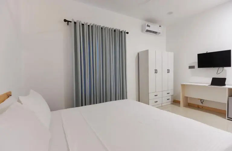 Einfaches Schlafzimmerinterieur im Splendour Grand im Ari-Atoll mit weißen Möbeln, Vorhängen, Kleiderschrank und Fernseher.