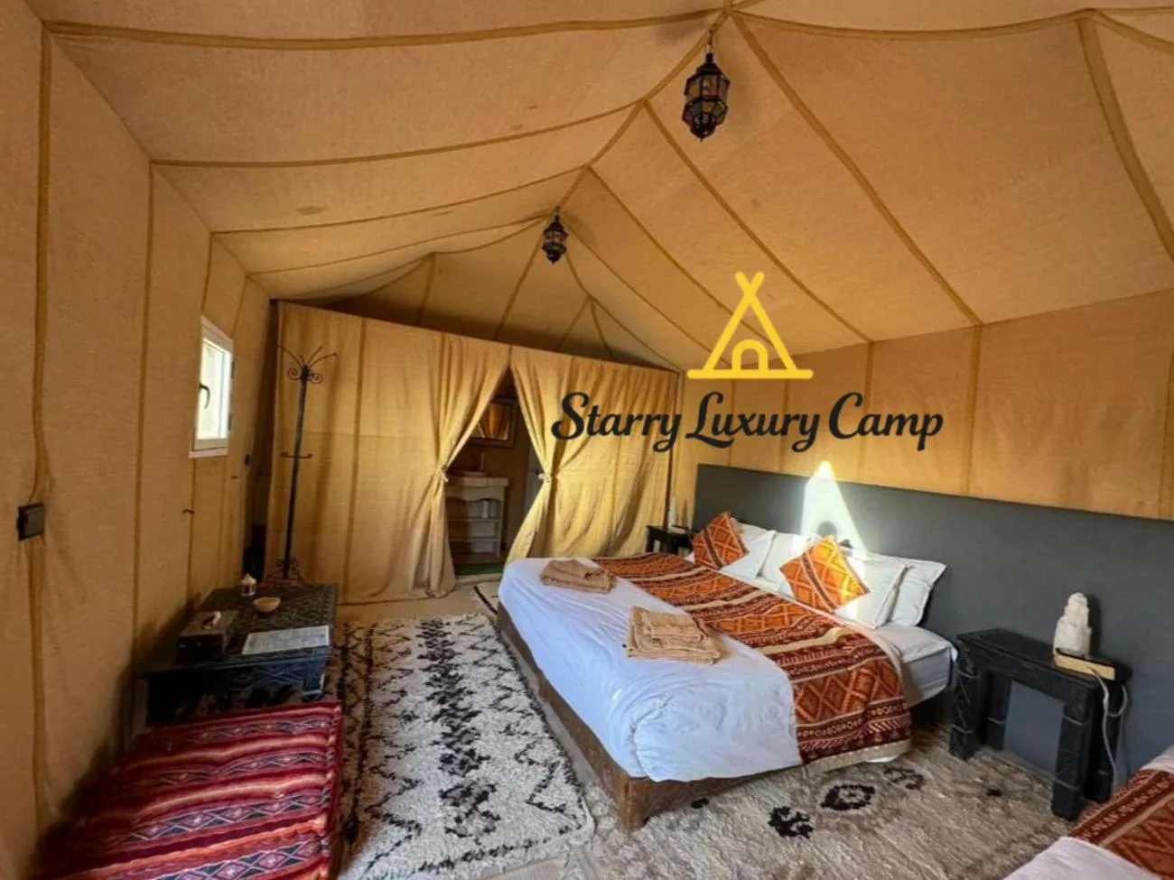 Suite premium de tienda en STARRY LUXURY CAMP en Merzouga con una cama king, alfombra estampada y zona de estar.