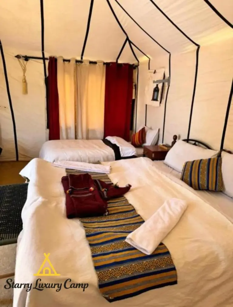 Habitación de huéspedes con dos camas en STARRY LUXURY CAMP en Merzouga con cortinas rojas y detalles tradicionales.
