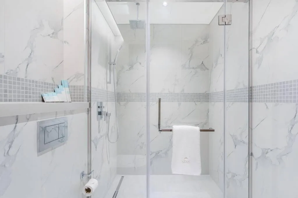 Baño con ducha de cristal en STAY BY LATINEM Luxury 1BR Holiday Home OPA2410 near Burj Khalifa en Dubai con paredes de aspecto marmolado.