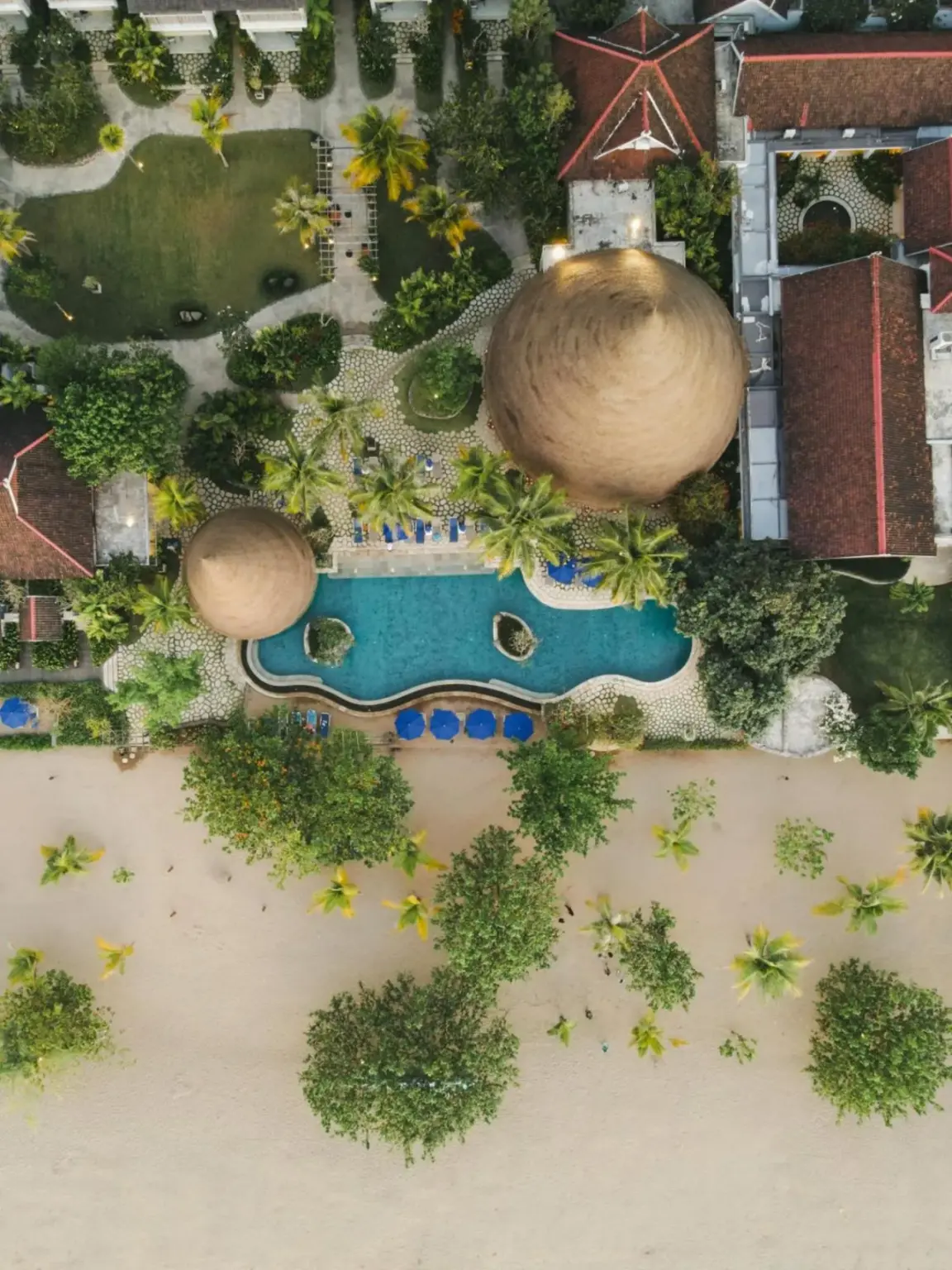 Luftaufnahme des Poolbereichs des Sudamala Resort in Labuan Bajo, die die schöne Bepflanzung und den Strand zeigt.