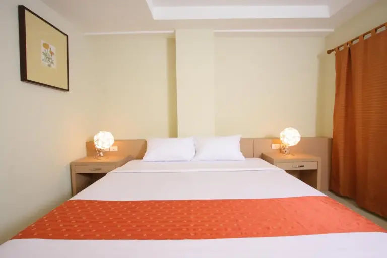 Vista frontal de una cama de huéspedes en Sunday Platinum Suites Bangkok con cubrecama naranja